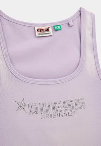 Top in tinta lilla a coste con scollatura rotonda, caratterizzato da scritte in strass argentati "GUESS ORIGINALS" e un'etichetta ecologica verde all'interno.