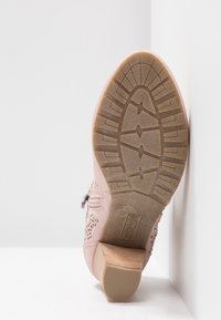 Pink heeled boot with perforated design and metallic accents. Textured rubber sole features a stable heel and patterned tread.