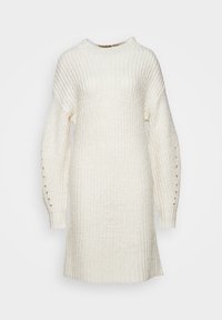Robe-pull en maille crème avec manches longues, dotée d'un col montant, d'une texture côtelée, et de trous d'accentuation verticaux sur les manches.