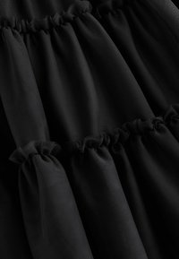 Gros plan d’un tissu noir froncé avec des coutures plissées créant des plis texturés verticaux.