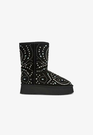 Black suede boot with sparkling studs and turquoise accents, featuring a rounded toe and a thick black platform sole. Textured surface details.