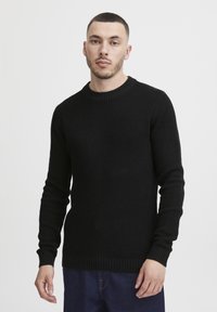 Suéter negro de punto con un escote redondo acanalado, tejido texturizado, mangas ajustadas y dobladillo recto, combinado con pantalones de denim.