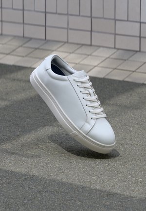 Baltas ādas sporta apavi ar gludu virsmu, šņorējams dizains un noapaļota purngala forma. Piedāvā teksturētu gumijas zoli un minimālistiskas detaļas.