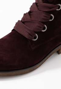 Bordowy zamszowy botek na kostkę z zaokrąglonym noskiem, teksturowanymi sznurowadłami, metalowymi oczkami oraz gumową podeszwą z subtelnym brązowym akcentem.