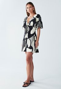Schwarz-weiß gemustertes kurzes Kleid mit tiefem V-Ausschnitt, kurzen Ärmeln und Kordelzug-Detail an der Taille. Glatte Stofftextur.