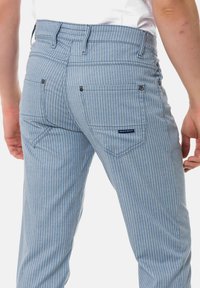 Gestreifte blaue Hose mit einer taillierten Passform, die zwei Gesäßtaschen, subtile Nähdetails und metallische Akzente aufweist.
