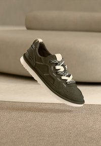 Σκούρο πράσινο σουέντ αθλητικό παπούτσι με λευκές λεπτομέρειες, κορδόνια με σχέδιο και υφή στη σόλα. Διαθέτει τρύπες για αερισμό και μαξιλαράκι στο πέλμα.