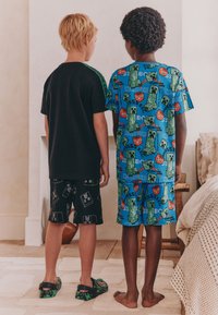 To børn står ryg mod ryg, den ene iført en sort T-shirt og shorts med et pixeleret mønster, den anden i en blå mønstret skjorte og shorts.