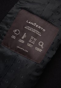 Czarna tkanina z wytłaczanymi wzorami, z brązową metką informującą o mieszance wełny, komforcie termicznym, elastycznej tkaninie i dbałości o szczegóły.