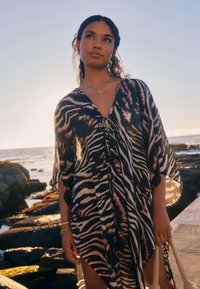 Schwarz-beiger Kaftan mit Zebramuster, V-Ausschnitt, offenen Ärmeln und Bindegürtel, aus leichtem Stoff, der elegant fällt.