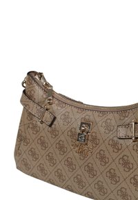 Bolso beige con un patrón de monograma texturizado, herrajes dorados, cierre de cremallera y una correa lateral para llevar.