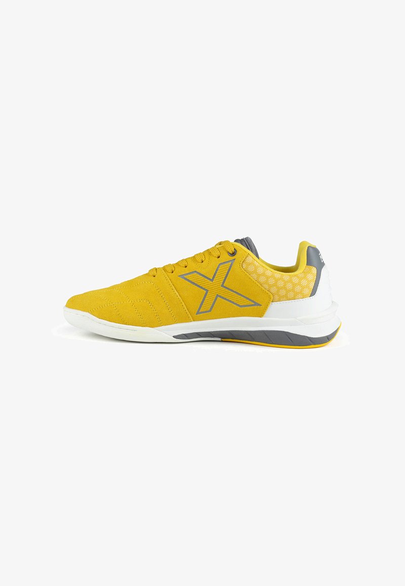 Chaussure de sport jaune et grise à lacets, grand logo "X" sur le côté, et semelle blanche avec des accents gris et jaunes.