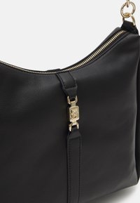 Bolso de hombro de cuero negro con una superficie texturizada, acento de cremallera dorada y un detalle de hardware dorado en la correa.