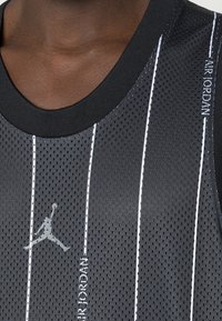 Camiseta de baloncesto de malla negra con rayas verticales blancas, cuello redondo negro y un logo de Jumpman gris en el frente.