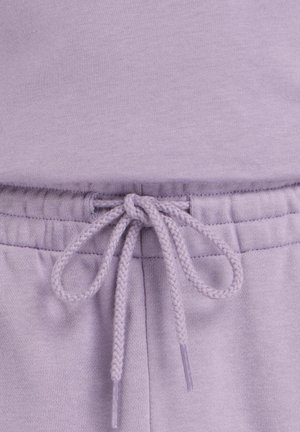 Primo piano della vita di pantaloni della tuta color lavanda con coulisse intrecciata annodata e cuciture elastiche a coste.