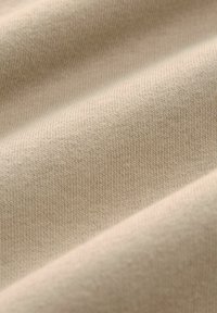 Tejido de algodón beige con una fina textura acanalada, que presenta suaves pliegues y un acabado liso, resaltando su elasticidad y caída.
