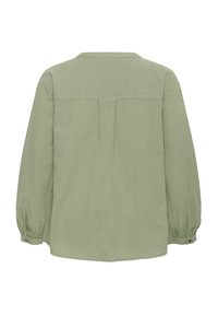 Blouse vert clair à manches longues avec poignets froncés et détail de couture sur le haut du dos, vue de dos.