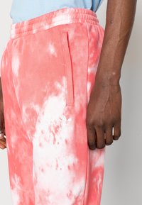 Rosa och vit tie-dye sweatpants med resårmidja och snörning samt sidoficka. Har vit Adidas-logotyp på vänster ben.