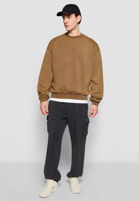 Brun oversized sweatshirt, blød tekstur, ribbede manchetter og kant. Kombineret med mørk cargo-bukser, der har sidelommer, og hvide sneakers.