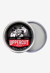 Latta in metallo contenente un prodotto per capelli in argilla grigia. Illustrazione in bianco e nero di un pugile sul coperchio con il testo rosso "UPPERCUT". Peso netto 70g.