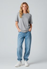 T-shirt gris à manches courtes associé à un jean bleu clair ample et des baskets blanches. Le t-shirt a un col rond et des manches retroussées.