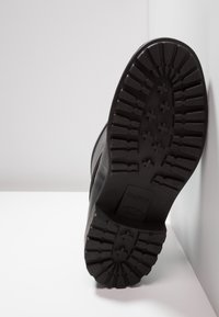 Zwarte rubberen laarszool met diepe profielgroeven en een lichte kromming. Voorzien van een opgedrukte logo en maatmarkeringen voor een stevige grip en duurzaamheid.