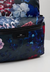 Kukkakuvioinen kangasreppu tummansinisillä, punaisilla ja valkoisilla kukilla, jossa on etutasku ja vetoketju, jossa lukee "DAY Birger et Mikkelsen."