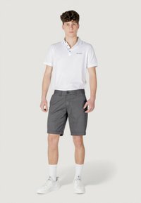 Polo bianco con colletto a tre bottoni, pantaloni corti grigi a scacchi e scarpe da ginnastica bianche con dettagli testurizzati e calzini a coste.