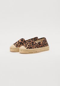 Espadrilles à imprimé léopard avec des panneaux élastiques sur les côtés, des semelles en jute et un bout arrondi. Les couleurs principales sont le noir, le marron et le beige.
