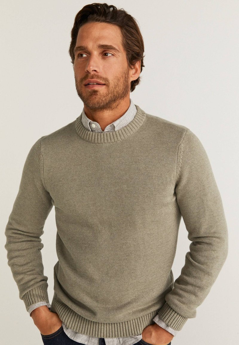 Pull en maille gris avec un col et des poignets côtelés, porté par-dessus une chemise légère à col. Tissu texturé, conception décontractée.