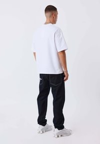 Camiseta blanca de manga corta combinada con vaqueros azul oscuro que tienen bolsillos traseros y costuras blancas, completada con zapatillas deportivas blancas.