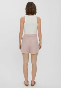 Ljusrosa shorts i mjukt tyg med en enkel design, med hög midja och bakfickor. Bärs med en vit linne.