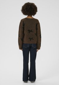 Brauner gestrickter Pullover mit schwarzen Vogelmustern, mit rundem Halsausschnitt und langen Ärmeln, kombiniert mit dunklen Schlagjeans.