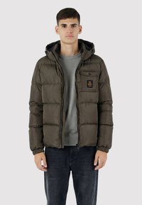 Giacca imbottita verde oliva, con chiusura a zip e cappuccio. Presenta polsini elastici e una tasca sul petto con dettaglio logo.