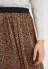 Falda plisada de estampado de leopardo con cinturilla elástica negra, en tonos de marrón, negro y naranja, fabricada en un tejido suave y texturizado.
