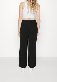 Schwarze weit geschnittene Hose mit einem elastischen Bund, aus einem glatten Stoff hergestellt. Kombiniert mit einem figurbetonten weißen Crop-Top und weißen Schuhen.