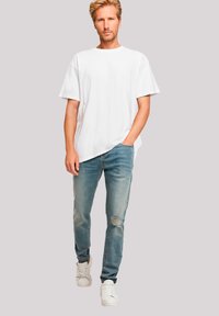 White cotton t-shirt paired with light blue denim jeans featuring distressed detailing. Model wearing white sneakers, standing against a neutral background.