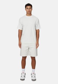 T-shirt gris clair à manches courtes et short assorti, avec des coutures contrastées, associé à des chaussures de sport blanches et noires.