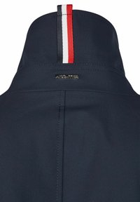 Marineblaue Jacke mit einem Kragen, der über vertikale Streifen in Rot, Weiß und Blau verfügt. Über der Naht befindet sich ein metallisches Branding. Der Stoff hat eine glatte Textur.