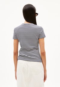 Randig t-shirt i marinblått och vitt, kortärmad, figurnära design, med en ribbad textur. Sedd bakifrån, i kombination med en vit kjol.