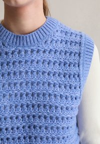 Jasnoniebieski dziergany kamizelka z fakturowanym wzorem, z otwartymi oczkami oraz prążkowanym okrągłym dekoltem. Tekstura dodaje wymiaru i głębi.