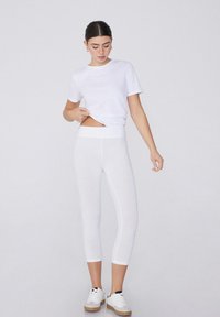 Witte katoenen T-shirt gecombineerd met witte capri-legging, met een gladde textuur en een hoge tailleband, afgemaakt met witte sneakers.