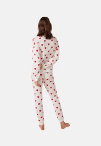 Witte sweatshirt en broek set met een rood hartpatroon. Zacht materiaal, losse pasvorm, geribde manchetten en enkels.
