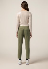 Stickad tröja med en ljusrosa, glänsande yta, tillsammans med gröna byxor med rak skärning och två bakfickor. Vita sneakers fulländar looken.