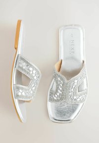 Sandales argentées à enfiler avec un bout carré, une bride découpée ornée de perles, et une semelle beige, présentées vues de dessus et de côté.