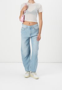 Camiseta corta blanca transparente, jeans de pierna ancha azul claro, zapatillas beige, sosteniendo un pequeño bolso rosa. Diseño simple con costuras visibles.