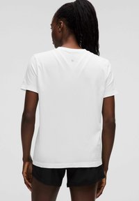 Weißes Kurzarm-Performance-T-Shirt mit strukturiertem Stoff und rundem Ausschnitt, kombiniert mit schwarzen Shorts. Dezentes Logo am Nacken.