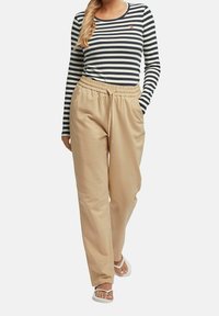 Svart och vit randig ribbad topp med lång ärm, ihop med beiga byxor med elastisk midja. Modellen bär vita flip-flops.