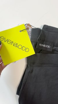 Temno sivi raztegljivi hlače z gladko teksturo, ki imajo črno oznako blagovne znamke in svetlo rumeno oznako s tiskom "even & odd".