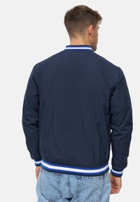 Marine bomberjakke med hvid og blåstribede ribkant og manchetter; glat stof; let polstret; elastisk talje; afslappet pasform.